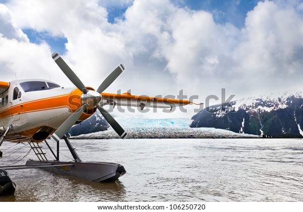 Seaplane or float plane in Alaska. The\
plane has landed under stormy skies near a\
glacier.