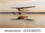 A seaplane float plane floats on a lake at sunset, the aircraft reflects in the calm waters of Candle Lake, in Northern Saskatchewan, Canada