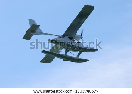 Seaplane (hydroplane or floatplane) flying in blue sky closeup. Cabin, wings propeller, engine, tail of plane are visible in details.
