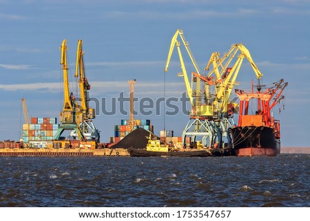 Seaport in the Arctic. A cargo ship near the pier of the sea port. Large port cranes. Logistics, shipping and freight in the Arctic. Stevedore services. Anadyr seaport, Chukotka, Far East Russia.