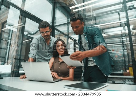 Searching for solutions. Group of three young and positive employees using modern technologies and discussing something while working in modern office