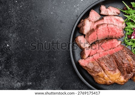 Seared beef chuck eye roll steak medium rare with fresh salad leaves. Restaurant style cooked beef on dark plate