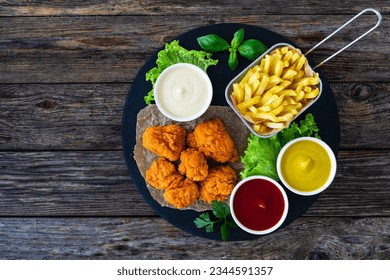 Seared breaded chicken nuggets with French fries on wooden table 