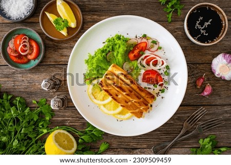 Seared calamari steak with lemon and fresh vegetables on wooden table 