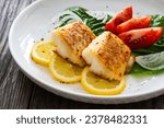 Seared cod loin and fresh vegetables on wooden table 