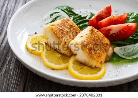 Seared cod loin and fresh vegetables on wooden table 