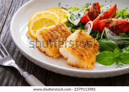 Seared cod loin and fresh vegetables on wooden table 
