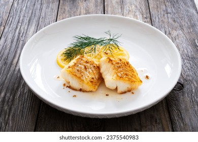 Seared cod loin and sliced lemon on wooden table 