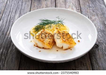 Seared cod loin and sliced lemon on wooden table 