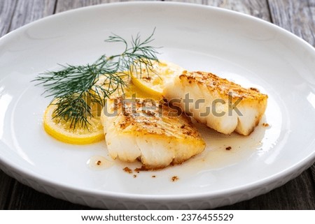 Seared cod loin and sliced lemon on wooden table 