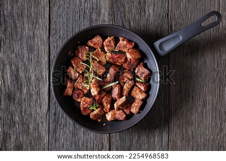 seared juicy new york strip steak bites with butter, rosemary and garlic on skillet on dark wood table, horizontal view from above, flat lay, copy space
