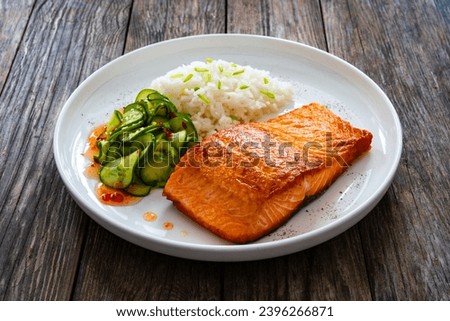 Seared salmon steak with boiled white rice and sliced cucumber on wooden table 