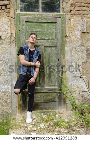 Searious guy is stangding at thi old green door.