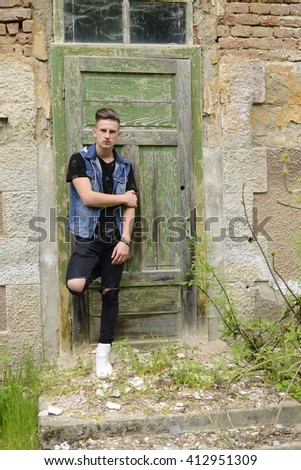 Searious guy is stangding at thi old green door.