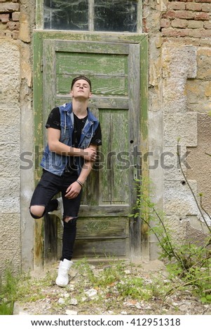 Searious guy is stangding at thi old green door.