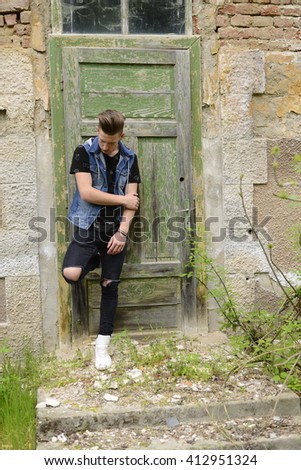Searious guy is stangding at thi old green door.