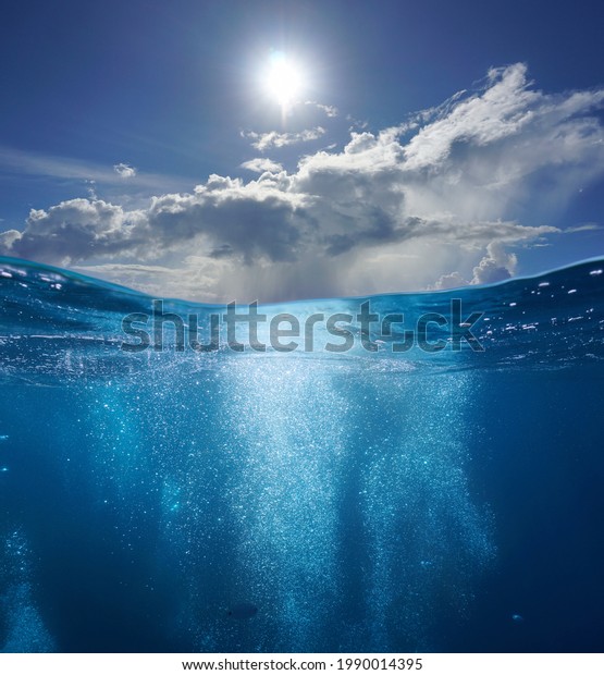 Seascape, air bubbles\
underwater sea and sunny blue sky with cloud, split view over and\
under water surface