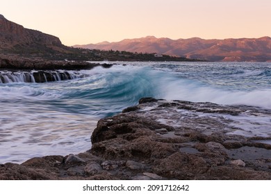 Seascape with blurred waves, rocky beach and sunset mountains, Monemvasia, Greece