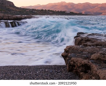 Seascape with blurred waves, rocky beach and sunset mountains, Monemvasia, Greece