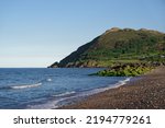 Seascape with the calm Irish Sea, pebble beach and rocks on sunny summer day in Bray, County Wicklow, Republic of Ireland. Famous Bray Head mountain in the background.