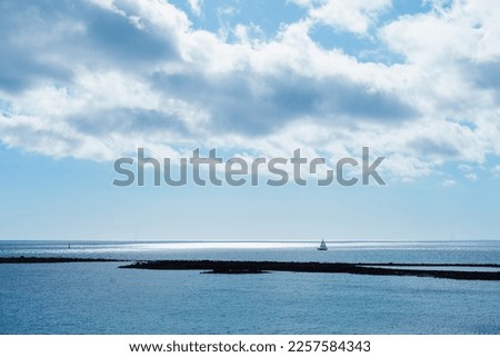 Seascape and cloudscape in blue color. Calm sea on a sunny day with clouds horizontal landscape background.  Distant boat silhouette in the ocean.