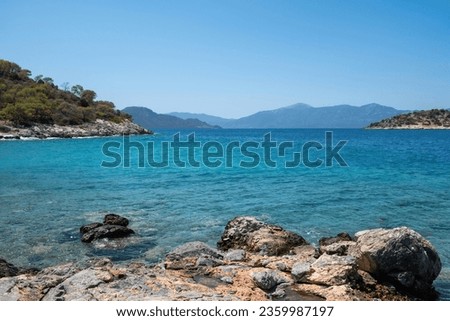 Seascape concept. Greece Aponisos beach destination Agistri island. Rocky land, pine tree, clear vast sea water, blue sky background. Summer vacation.