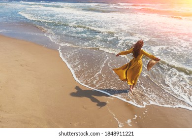 Seascape on a sunny day in summer. Woman on the beach, summertime. Young happy woman with hands in the air walks carefree on the seaside in yellow fluttering dress. View from above - Powered by Shutterstock