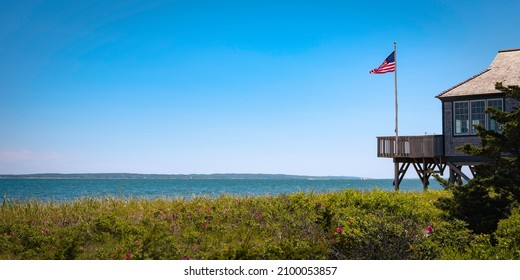 Seascape Over Martha's Vineyard In Summer With The View Of Waving American Flag And Beach House In Partial View. Tranquil Coastal Landscape On Cape Cod.