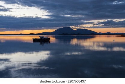 Seascape Photo: Old Wooden Fishing Boat At Still Sea At Sunset, Mountain And Clouds Reflecting On Water Surface. Summer Midnight In Nordland, Norway. 