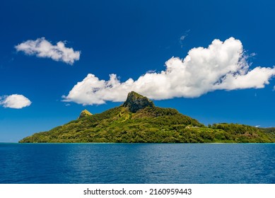 Seascape photo of remote island of Mangareva in the Gambier Archipelago of French Polynesia, South Pacific, blue sky and beautiful volcanic mountain covered in tropical vegetation