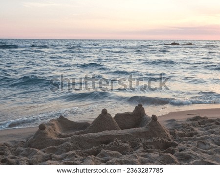 Seascape. Sand castle, sea, water and sky background. Mediterranean Sea landscape. Sunset on Italy, Campania. Coastline with sand castle and sand. Sunset water and pink sky. Pink sun light over sea.