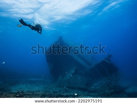 Seascape of a scuba diver approaching a ship wreck in the distance