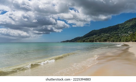 Seascape. The turquoise ocean is calm. The waves roll beautifully on the sandy beach. A green hill against a background of blue sky and clouds. Seychelles. Mahe. Beau Vallon - Shutterstock ID 2225394883