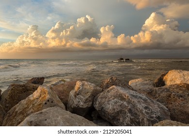 Seascape in Tuscany during the golden hour after a storm. A Trabucco (fishing mashine) in the background. Clouds in the sky. Rocks on the foreground