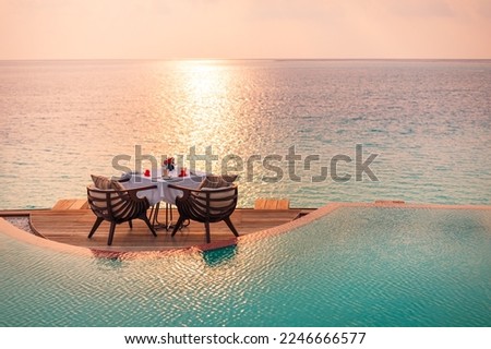 Seascape view under sunset light with dining table with infinity pool around. Romantic tranquil getaway for two, couple concept. Chairs, food and romance. Luxury destination dining, honeymoon template