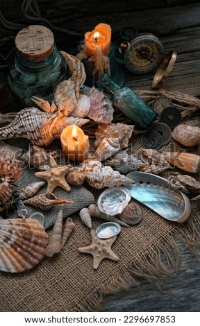 seashells, burning candles, old bottles, retro compass on table close up, dark abstract background. theme of pirates, adventure. vintage composition. symbol of journey, sea vacation, travel, tourism.