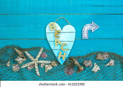 Seashells, Starfish And Fish Net Border On Antique Rustic Teal Blue Wood Background With Metal Direction Arrow; Broken Heart Beach Sign