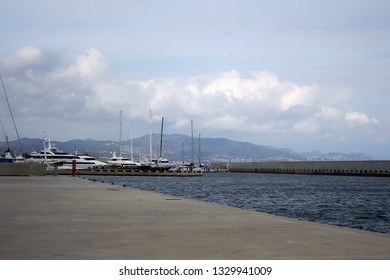 Seashore perspective with ships in the background surrounded by mountains and clouds in the distance - Powered by Shutterstock