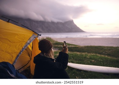 Seaside, camping and woman with picture, sunset and capture moment with adventure. Person, beach and surfer with smartphone, journey and getaway trip with travel vlogger, photo and holiday with app - Powered by Shutterstock