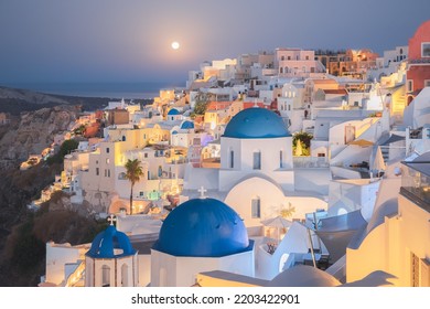 Seaside Moonlit View At Night Of Traditional White Wash Buildings And Blue Dome Churches At The Popular Seaside Tourist Resort Village Of Oia On The Greek Island Of Santorini, Greece.