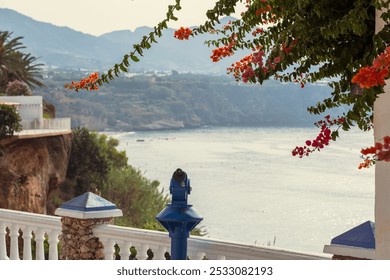 A seaside resort in Spain. In the foreground, red flowers and a viewing platform with binoculars, in the background, a blurred seascape. - Powered by Shutterstock