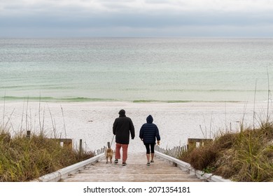 Seaside, USA - January 10, 2021: Couple people with dog walking in Seaside, Florida gulf coast beach with wooden boardwalk steps down and white sand with colorful emerald water