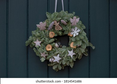 Season Greeting Theme, Christmas Wreath Made From Green Pine Tree Assortment Of Flowers Hanging On Front Door, Xmas Ring Decoration With On Wooden Background.