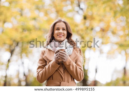 season, hot drinks and people concept - beautiful happy young woman drinking coffee or tea from disposable paper cup in autumn park