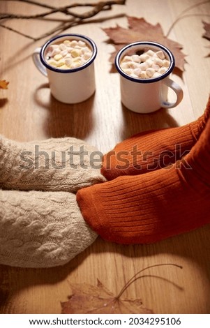 season and leisure concept - couple of coffee cups, autumn leaves and feet in socks at home