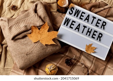 season and objects concept - wool clothes, autumn leaves, glasses and light box with sweater weather letters on warm blankets