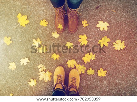 season and people concept - couple of feet in boots with autumn leaves on ground
