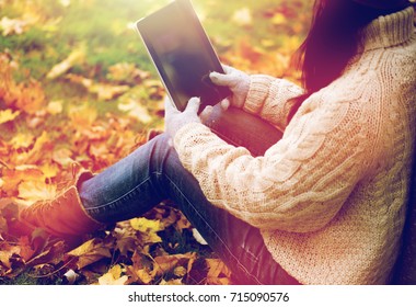 season, technology and people concept - close up of young woman with tablet pc computer sitting on grass in autumn park - Powered by Shutterstock