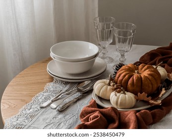 Seasonal autumn table setting - a plate with decorative pumpkins, cones, dishes, glasses on a round wooden table - Powered by Shutterstock