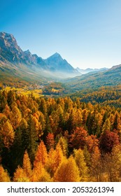 Seasonal autumnal scenery in Dolomite Alps, Cortina d'Ampezzo, Italy. Sunny day with yellow larches below and valley covered by fog and high mountains behind. Popular travel destination in autumn